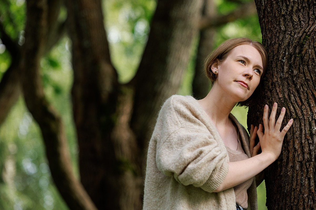 Nainen nojaa puuhun.